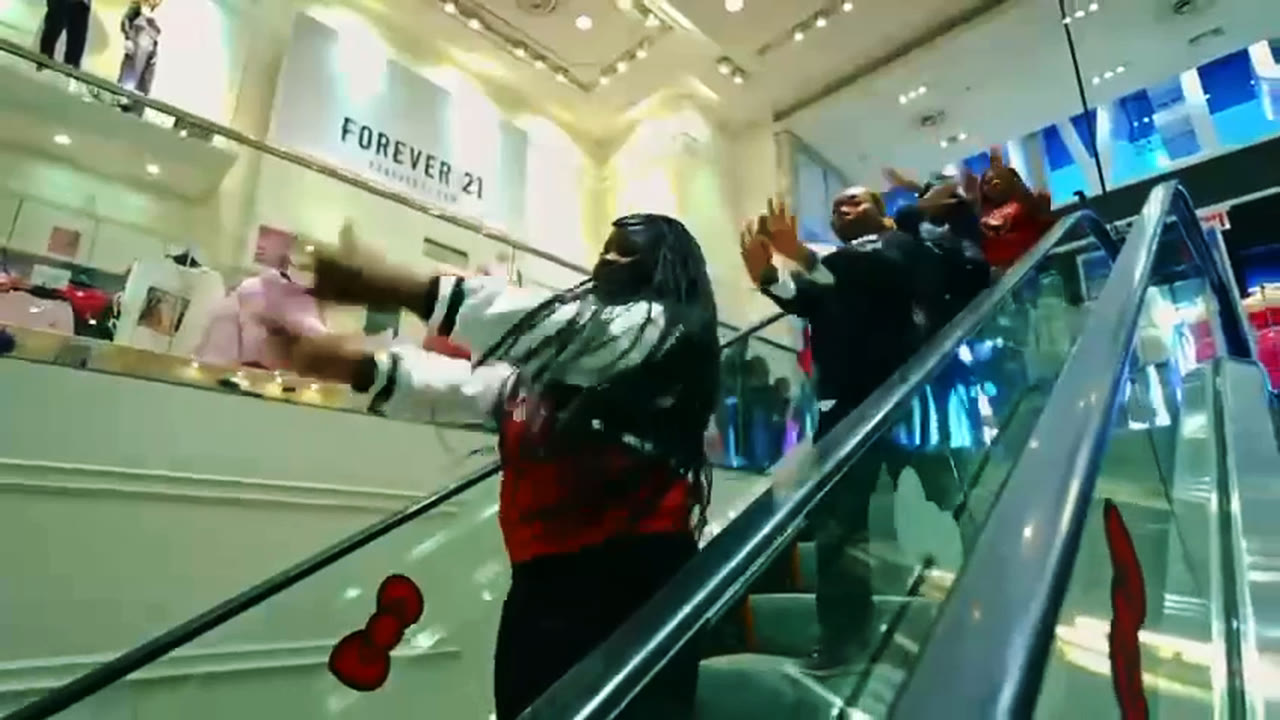 A dancer in a red varsity jacket strikes a pose riding down a mall escalator